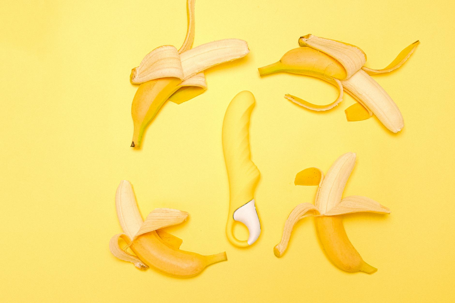 Yellow lemon vibrator surrounded by fresh lemons on a bright yellow background.