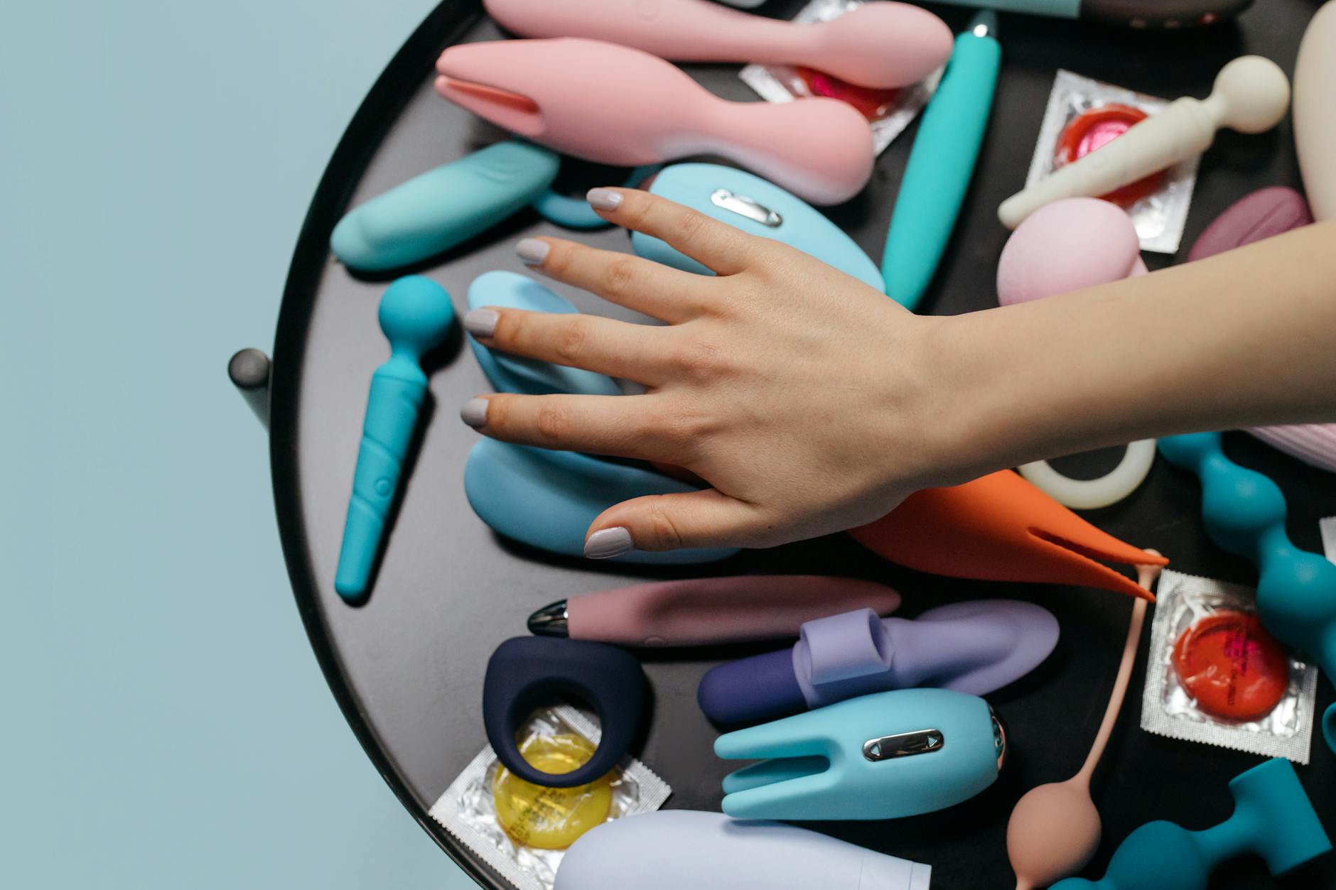 Two hands holding pink and blue silicone vibrators against a pastel background.