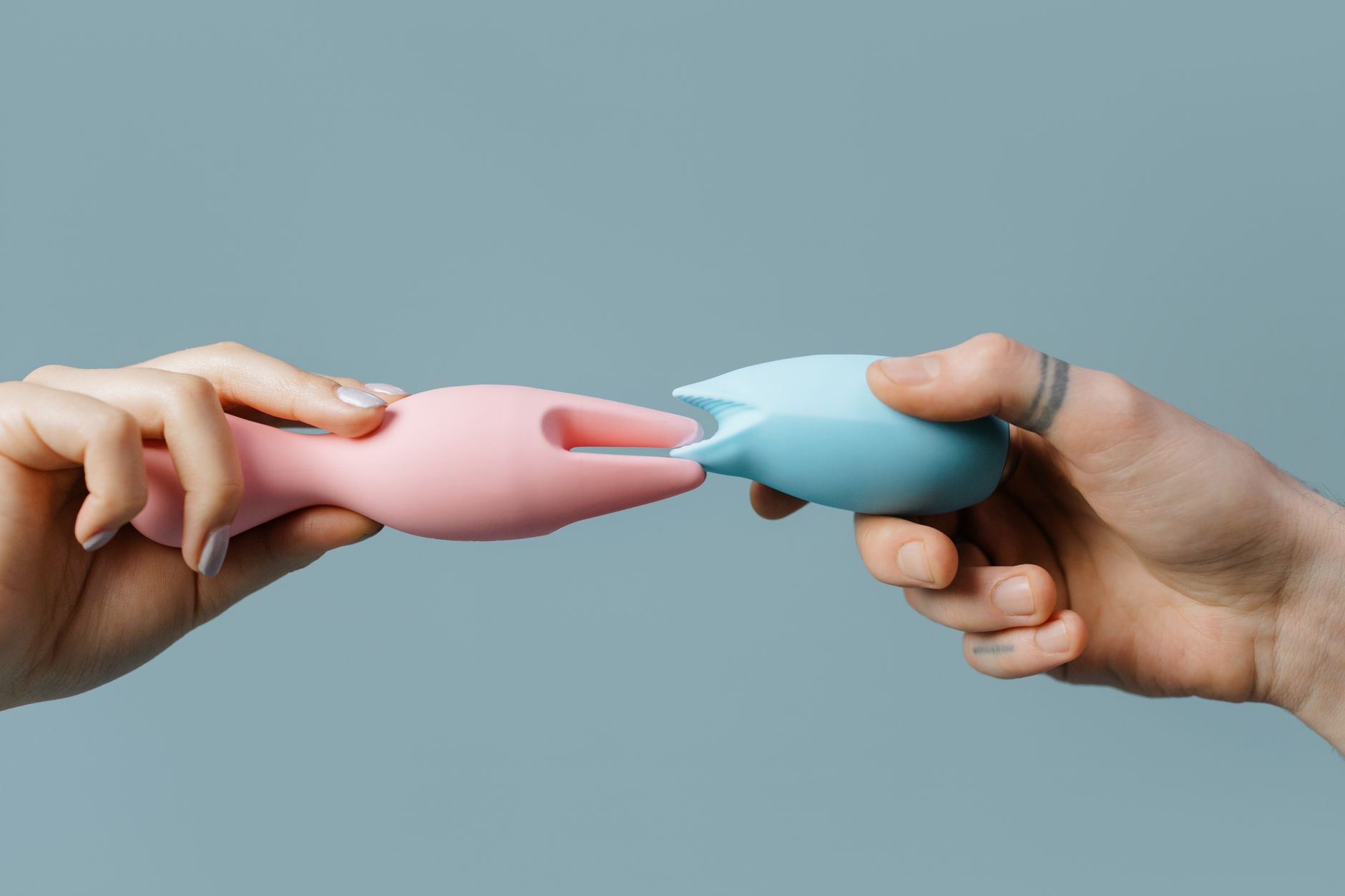Hands holding colorful silicone vibrators on a neutral background