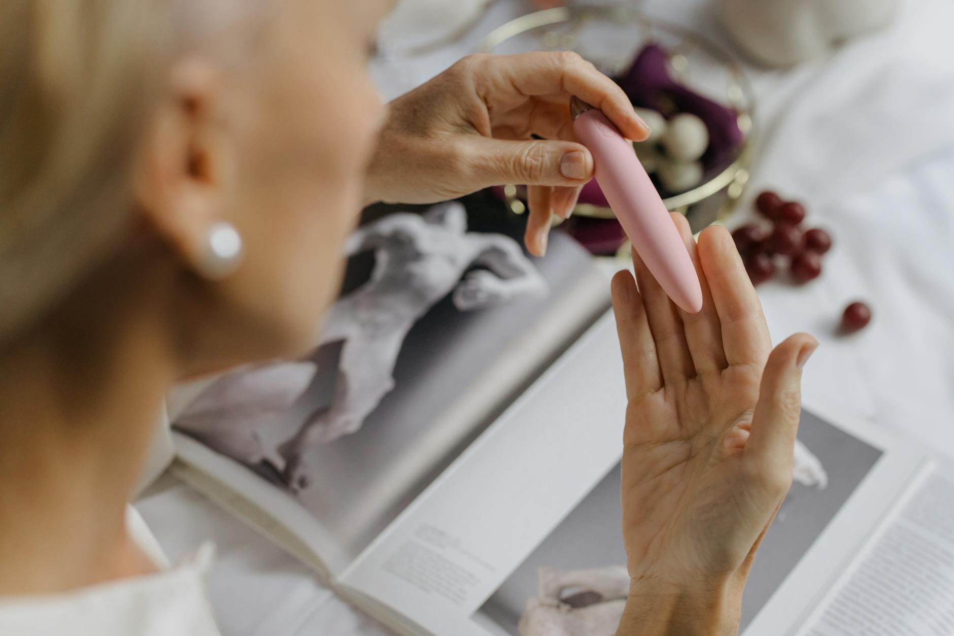 A close-up of a hand holding a pink vibrator with art books in the background
