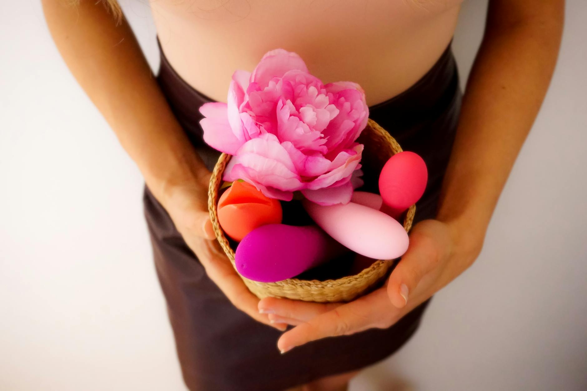 Hand holding a basket of colorful adult toys, representing the diversity of vibrator options and sensations available